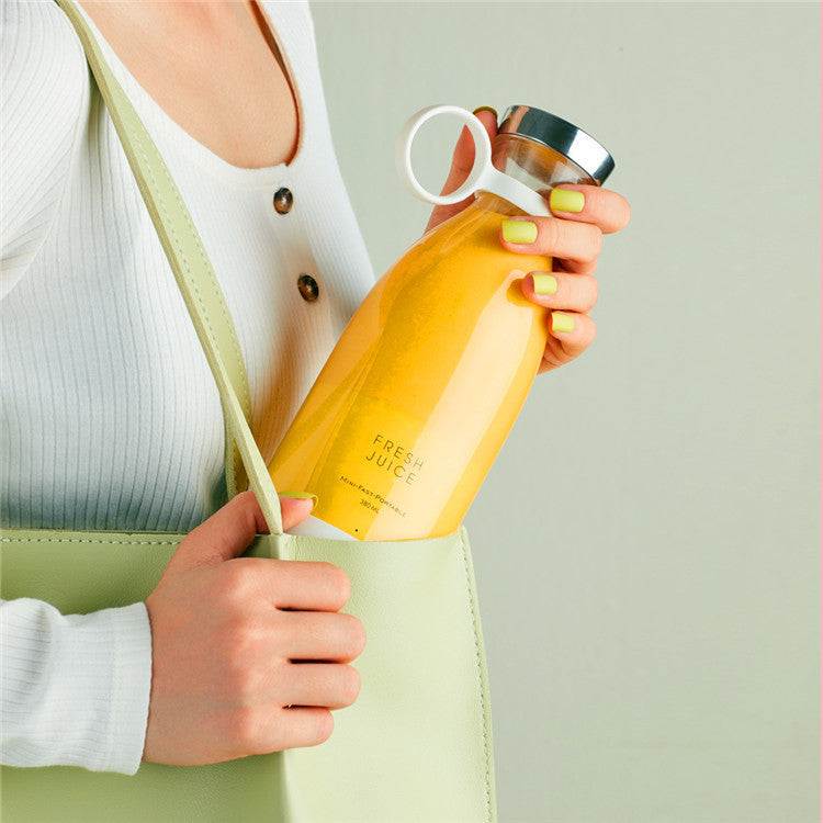 Portable Blendy Bottle blender with pink design next to a glass of juice, grapefruit, berries, and a palm leaf.
