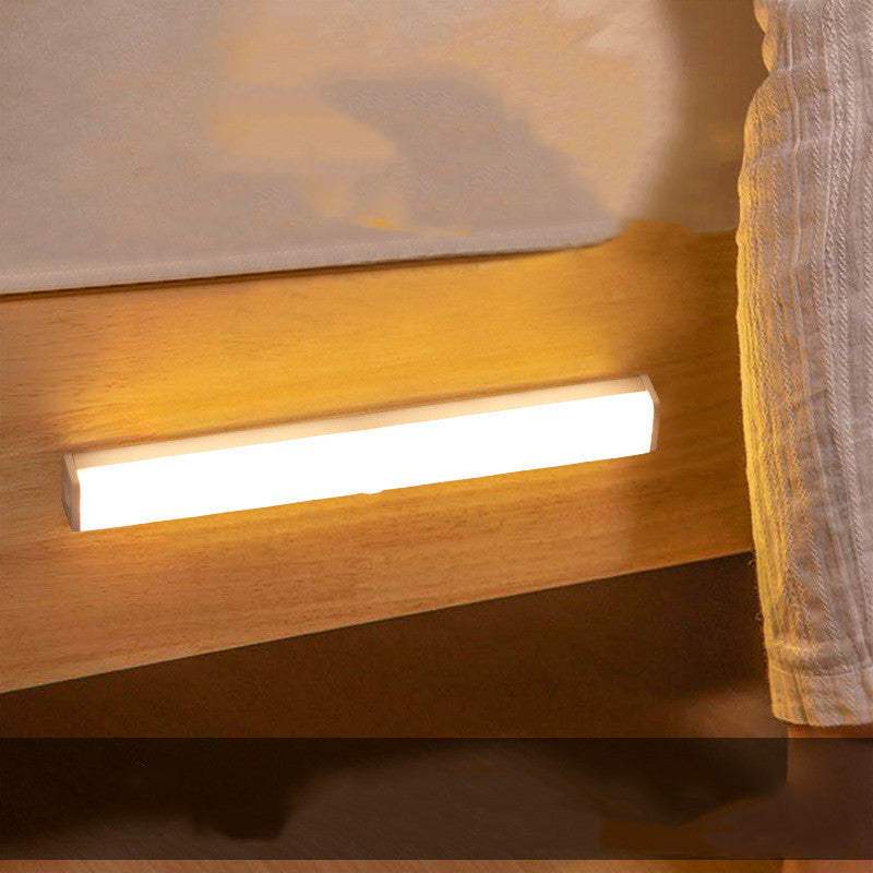 LED sensor light bar emitting warm light under a sofa.