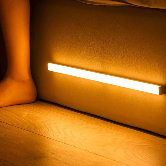 LED sensor light bar emitting warm light under a sofa.